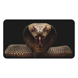 Puede incluir: Alfombrilla de ratón rectangular con una imagen detallada de una cobra. La serpiente tiene un cuerpo marrón y beige con patrones, ojos rojos y una lengua rosa extendida. El fondo es negro sólido.