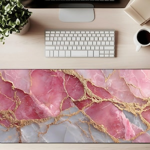 May include: A rectangular desk mat with a pink marble design and gold veining. The mat is on a wooden desk with a keyboard, monitor, coffee cup, and plant.