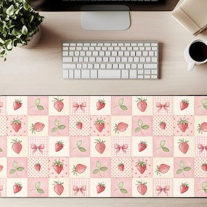 May include: A rectangular desk mat featuring a repeating pattern of strawberries, bows, and leaves on a pink and cream patchwork design. The mat is designed to protect the desk surface and provide a smooth surface for a mouse and keyboard.
