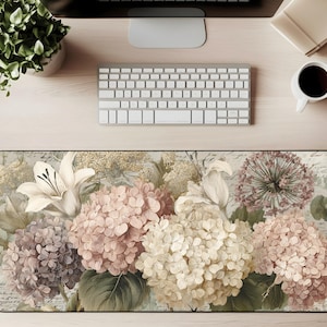 May include: A floral mouse pad featuring a vintage-style design with hydrangeas, lilies, and other flowers in shades of pink, cream, and purple. The rectangular pad is on a wooden desk with a keyboard and coffee cup.
