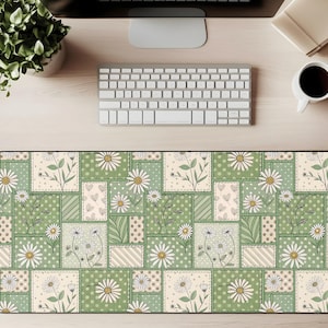 Könnte beinhalten: Rechteckige Schreibtischunterlage mit einem Patchwork-Design mit Gänseblümchen, Herzen und floralen Elementen in Grün-, Creme- und Beigetönen. Die Matte liegt auf einem hellen Holzschreibtisch, mit Tastatur, Monitor und Kaffeetasse.