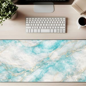 May include: A rectangular desk mat with a marble design. The mat features a pattern of white, teal, and gold swirls. The mat is on a light wood desk, with a keyboard, monitor, coffee cup, and plant visible.