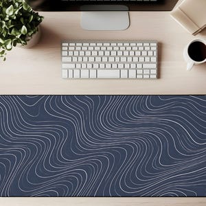 May include: A large, rectangular desk mat with a dark blue background and a white, wavy line pattern. The mat is designed to sit under a keyboard and mouse, providing a smooth surface for computer use. The design is modern and abstract.