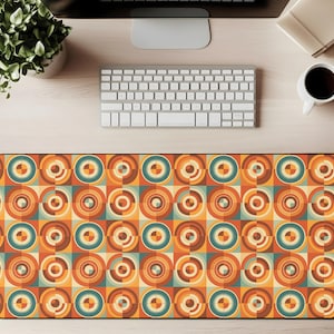 May include: A rectangular desk mat with a retro geometric pattern. The design features concentric circles in shades of orange, teal, and cream, arranged in a repeating square grid. The mat is designed to protect a desk surface.