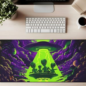 May include: A black rectangular mousepad featuring a vibrant illustration of a UFO beaming down a bright green light onto a group of green aliens. The background is a mix of purple and green clouds and planets.