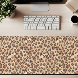 Könnte beinhalten: Rechteckige Schreibtischunterlage mit Leopardenmuster. Die Matte hat ein sich wiederholendes Muster aus braunen und schwarzen Flecken auf beigem Hintergrund. Die Matte soll eine Schreibtischoberfläche schützen und eine glatte Oberfläche für Maus und Tastatur bieten.