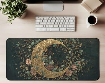 May include: A rectangular desk mat with a gold crescent moon design surrounded by flowers and foliage in green, pink, and gold. The mat is on a light wood desk with a keyboard, monitor, and coffee cup.