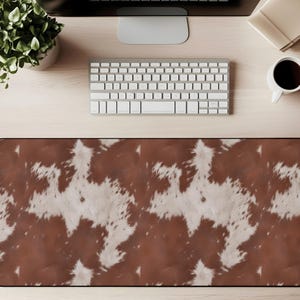 May include: A rectangular desk mat with a brown and white cowhide pattern. The mat is designed to protect the desk surface and provide a smooth surface for a mouse and keyboard. The mat is surrounded by a black border.
