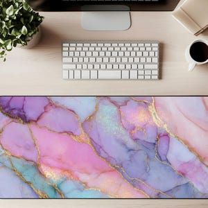 May include: A rectangular desk mat with an abstract design in shades of pink, purple, and teal, with gold vein detailing. The mat is designed to protect the desk surface and enhance the workspace, and measures approximately 80 cm in length.