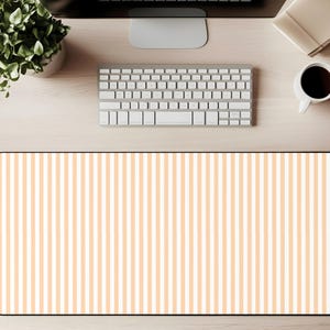 May include: A rectangular desk mat with a pattern of vertical peach and white stripes. The mat is surrounded by a black border. A keyboard, coffee cup, and plant are visible on the wooden desk.