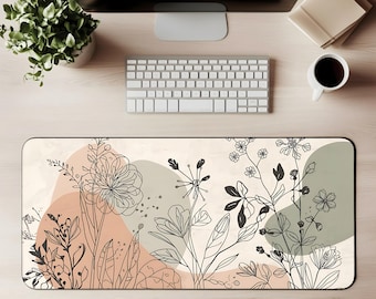 Può includere: Tappetino da scrivania rettangolare con un design floreale in arte lineare nera su uno sfondo neutro con forme pesca e verde salvia. Una tastiera, un monitor, una tazza di caffè e una pianta circondano il tappetino.
