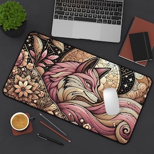 May include: A decorative desk mat featuring a stylized fox design in pink, cream, and gold tones. The fox is the central focus, surrounded by floral and geometric patterns. A white computer mouse rests on the mat.