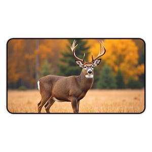 May include: A brown deer with large antlers stands in a field of dry grass. The background features a blurred forest with trees displaying vibrant autumn colors of yellow and orange. The deer has a white patch on its rear.