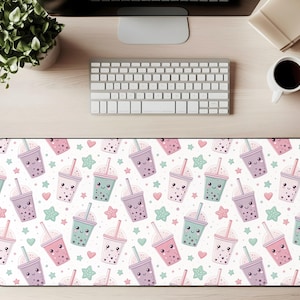 May include: A rectangular desk mat featuring a repeating pattern of cartoon bubble tea cups in pastel pink, purple, and teal. The design includes hearts and stars on a white background. The mat is designed to protect a desk surface.