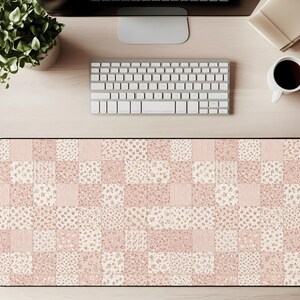 May include: A rectangular desk mat with a patchwork design in shades of pink and cream. The pattern features squares with floral, striped, and solid textures. The mat is designed to protect the desk surface.