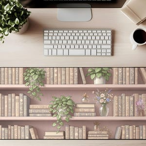 May include: A desk setup featuring a keyboard, coffee cup, and a decorative desk mat. The mat displays a bookshelf design with rows of books, potted plants, and floral arrangements. The color palette is soft, with pink shelves and neutral-toned books.