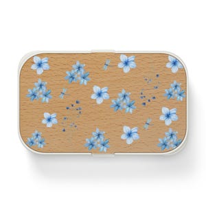May include: A rectangular container with a white frame and a light brown wooden surface. The surface is decorated with light blue watercolour flowers and dragonflies. Likely a lunch box or storage box.