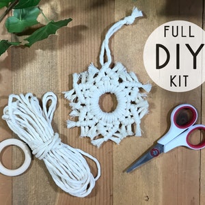 May include: A macrame DIY kit with a finished white macrame snowflake, a bundle of white rope, a wooden ring, and scissors. The kit includes the text "FULL DIY KIT" on a white circle.