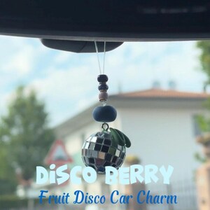 May include: A car charm featuring a disco ball fruit design. The charm has a reflective surface, green leaf accents, and is suspended by a string of beads. Text on the image reads "DISCO BERRY Fruit Disco Car Charm."