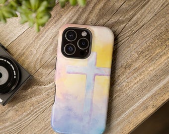May include: A phone case with a watercolor design featuring a cross. The case has a pastel color scheme with yellow, purple, and blue hues. The phone case is on a wooden surface.