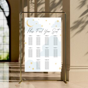 May include: A seating chart with a gold frame, featuring a celestial design with a crescent moon, clouds, and stars. The text "Please Find Your Seat" is displayed at the top, with table numbers and space for names below. The chart is set against a neutral background.