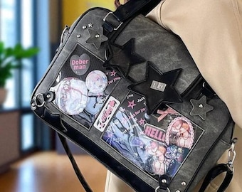 May include: Gray messenger bag with black trim, star accents, and clear pockets displaying colorful graphics and pins. The bag has a shoulder strap and metal hardware. The text "Dober man" is visible on a circular pin.