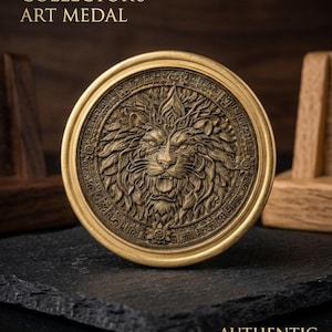 Puede incluir: Medalla de arte dorada con un diseño detallado de cabeza de león en el centro. La medalla es redonda y tiene el texto "LIMITED EDITION COLLECTOR'S ART MEDAL" en la parte superior y "AUTHENTIC HISTORICAL DESIGN" en la inferior.