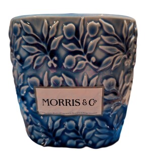 Puede incluir: Un recipiente de cer&aacute;mica azul con un patr&oacute;n floral en relieve. El recipiente tiene una etiqueta rectangular con el texto "MORRIS & Co". El dise&ntilde;o presenta hojas y flores estilizadas en un patr&oacute;n repetitivo.