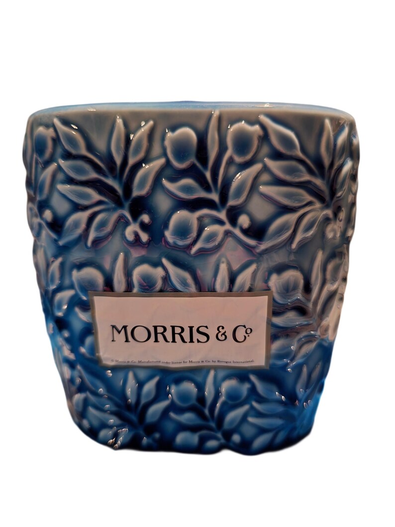 Puede incluir: Un recipiente de cer&aacute;mica azul con un patr&oacute;n floral en relieve. El recipiente tiene una etiqueta rectangular con el texto "MORRIS & Co". El dise&ntilde;o presenta hojas y flores estilizadas en un patr&oacute;n repetitivo.