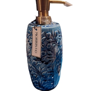Puede incluir: Un dispensador de jab&oacute;n de cer&aacute;mica azul con un dise&ntilde;o floral y una bomba dorada. El dispensador tiene una etiqueta que dice "MORRIS & Co."