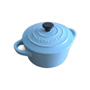May include: A light blue enameled cast iron round Dutch oven with a matching lid. The lid features a black knob and the embossed text LE CREUSET. The pot has two side handles and a smooth, glossy finish on the exterior surface.