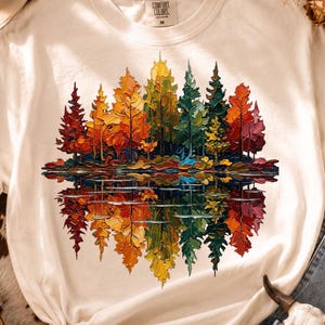 May include: An off-white short-sleeve t-shirt featuring a colorful graphic of a forest with trees in shades of red, orange, yellow, and green. The design includes a mirrored reflection of the trees below, creating a symmetrical landscape effect.