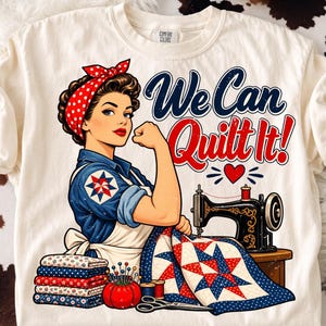 May include: A cream-colored t-shirt featuring a graphic of a person with a red polka-dot headscarf flexing an arm, next to a sewing machine and a quilt. The text reads We Can Quilt It! with a small red heart. Includes fabric stacks and scissors.