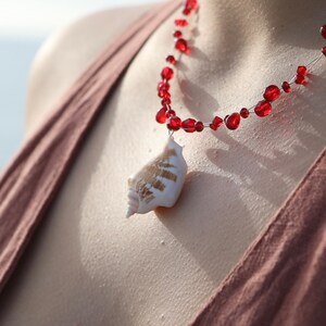 May include: A red beaded necklace with a seashell pendant. The necklace features small, round red beads strung on a thin wire. The pendant is a white and tan seashell.