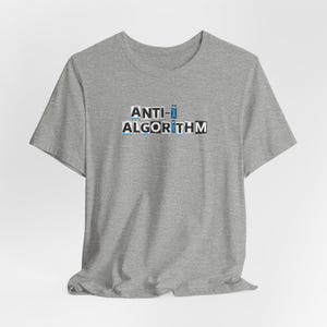 May include: A heather gray t-shirt with the words "ANTI- ALGORITHM" printed in a block letter style. The text is in white, black, and blue. The shirt has short sleeves and a crew neck.