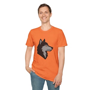 May include: Orange short-sleeve t-shirt featuring a wolf head graphic. The wolf graphic is in black and gray with an orange eye. The shirt is made of a soft material.