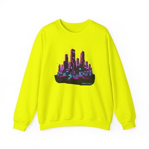 May include: A neon yellow sweatshirt featuring a graphic of a futuristic cityscape in shades of pink, purple, and blue. The design includes tall buildings and a glowing base. The text "40.8521 N 74.0061 W" is printed below the graphic.
