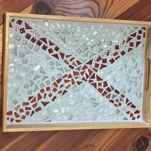 Könnte beinhalten: Ein rechteckiges Serviertablett aus Holz mit Mosaikdesign. Das Mosaik hat einen weißen Hintergrund mit einem roten und orangefarbenen Kreuzmuster. Das Tablett hat einen hellbraunen Holzrahmen und integrierte Griffe.