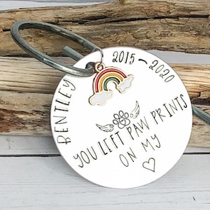 May include: A silver metal keychain with a rainbow charm and the text "Bentley 2015 - 2020 You Left Paw Prints On My Heart".