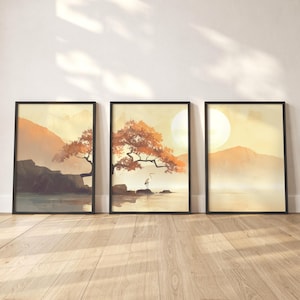 Puede incluir: Tres impresiones artísticas enmarcadas de paisajes. Cada impresión presenta una escena serena con montañas, agua y árboles en tonos cálidos de naranja, amarillo y marrón. La impresión del medio incluye un árbol y un pájaro.