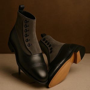 Puede incluir: Un par de botines negros y grises con cierre de botones. Los botines tienen un diseño de puntera y suela de madera. La parte superior del botín es de ante gris, mientras que la parte inferior es de cuero negro.