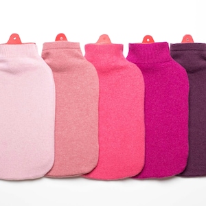 Peut inclure: Cinq bouillottes aux couleurs vives, allant du rose clair au violet foncé. Chaque bouillotte est recouverte d'une housse tricotée assortie et possède un bouchon rouge. L'ensemble est disposé sur fond blanc.