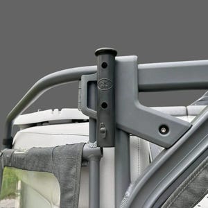 May include: A gray metal roll bar with a black vertical support. The support has a cylindrical top and several holes. The letters "AK BIX" are visible on the support. The roll bar is attached to a vehicle.