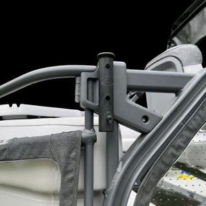 May include: Close-up of a gray metal stroller frame with a black background. The frame has a curved handlebar and a connecting bracket. The stroller's fabric is visible on the sides.