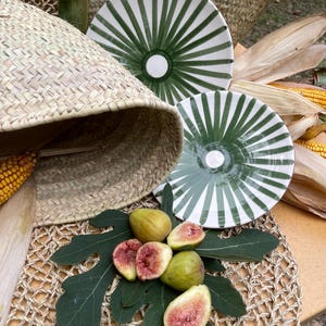 Puede incluir: Naturaleza muerta con platos estampados en verde y blanco, una cesta de mimbre y higos frescos. Los higos se exhiben sobre una hoja verde, con hojas de maíz y un salvamanteles tejido.