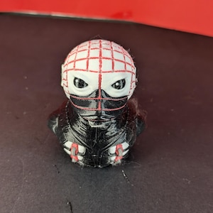 Könnte beinhalten: 3D-gedruckte Figur eines Charakters mit weißem Kopf mit rotem Gittermuster. Der Charakter hat schwarze Augen und eine schwarze Maske. Der Körper ist schwarz mit roten Akzenten. Die Figur steht auf einer dunklen Oberfläche.