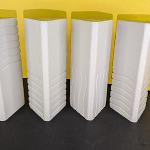 Puede incluir: Cuatro jarrones decorativos blancos y rectangulares con tapas amarillas. Cada jarrón tiene un diseño texturizado único en la parte delantera, que incluye patrones de ondas y geométricos. Los jarrones están dispuestos en fila sobre un fondo amarillo.