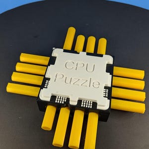 Puede incluir: Rompecabezas de CPU impreso en 3D con un componente central blanco y clavijas amarillas. El texto "CPU Puzzle" está impreso en el centro blanco. El rompecabezas está sobre una superficie negra con un fondo azul.