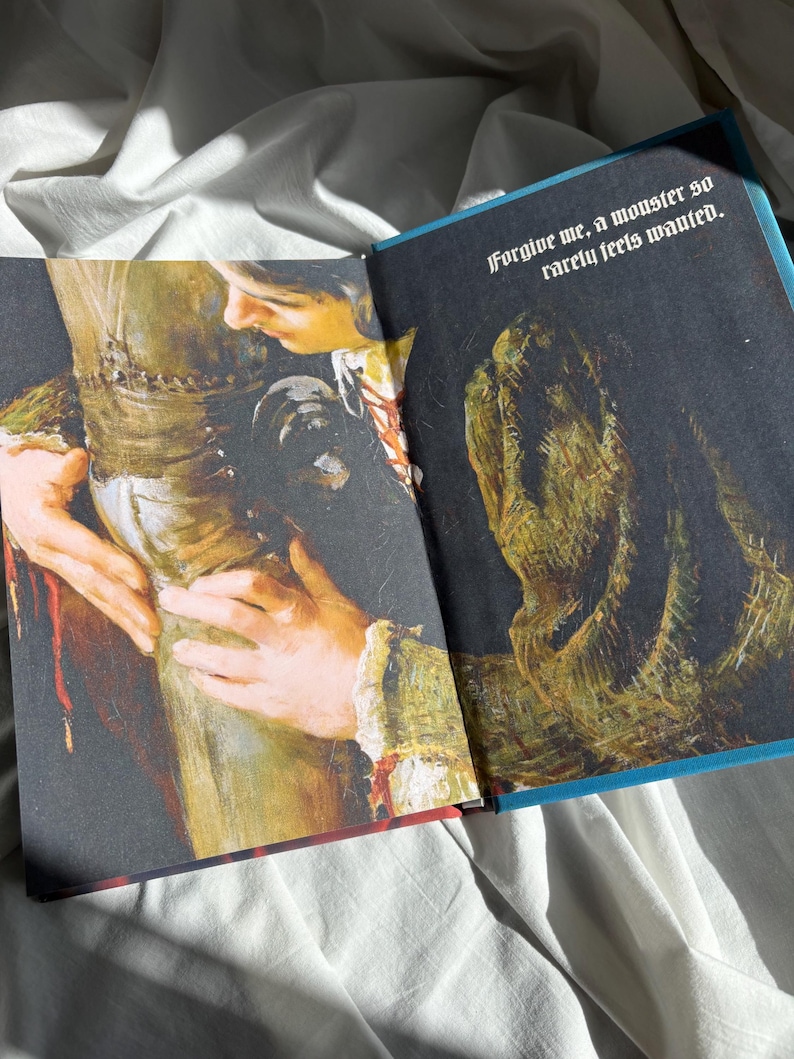 May include: An open book featuring an illustration of a person embracing a textured, dark green creature. The text printed in white at the top right corner reads, "Forgive me, a monster so rarely feels wanted." The artwork uses deep shadows and highlights.