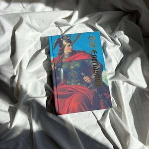 May include: A hardcover book titled The Everlasting featuring a vibrant illustration of a figure in ornate armor and a flowing red cloak, holding a spear and sword against a blue sky background, with gold lettering on the front cover.